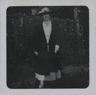 Untitled [Woman wearing hat stands in front of garden fence]