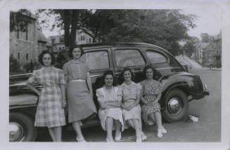 Untitled [Two women stand in front of car, three women sit on its side]