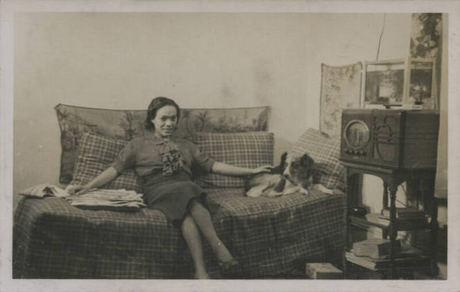 Untitled [Woman sits on bed, cross legged, reaches out to dog]