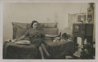 Untitled [Woman sits on bed, cross legged, reaches out to dog]