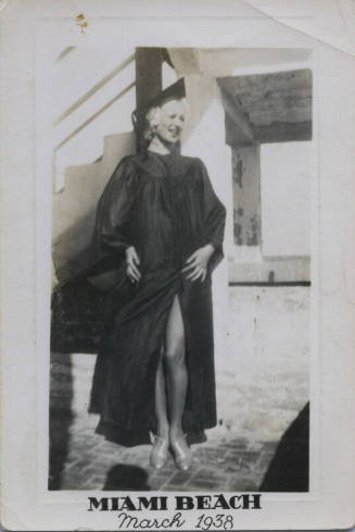 Untitled [Woman in graduation gown looks to one side, hands on hips]