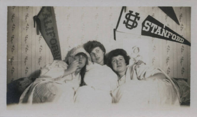 Untitled [Three women lie in bed, California and Stanford banners on wall]
