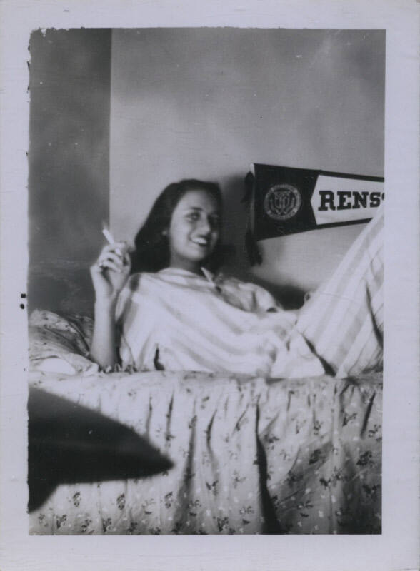Untitled [Woman lies on bed, cigarette in hand, banner reading Rens (perhaps Rensselaer) in background]