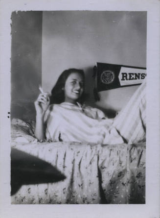 Untitled [Woman lies on bed, cigarette in hand, banner reading Rens (perhaps Rensselaer) in background]