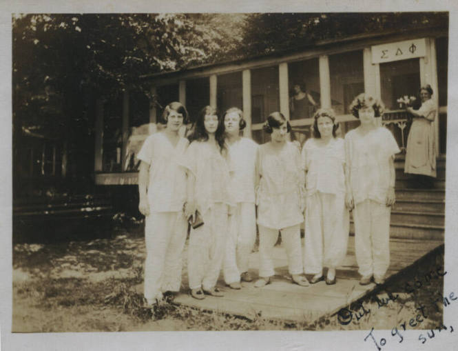 Untitled [Six women stand on porch, two women in background stand in house whose banner reads S?F (Sigma Delta Phi)]