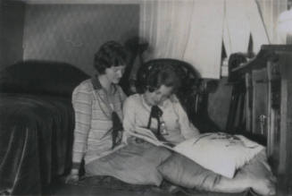 Untitled [Two women sit on floor and read book]