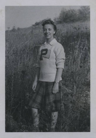 Untitled [Woman stands on field, wears sweater inscribed with letter P]