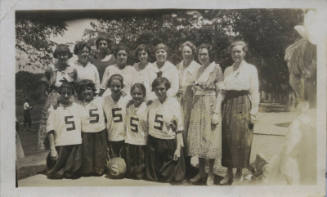 Untitled [Fourteen figures stand together, five people kneel wearing shirts that read 5, two figures on either side appear in the periphery]