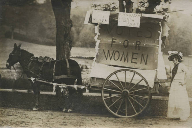 Untitled [Subject stands behind coach that reads VOTES FOR WOMEN]