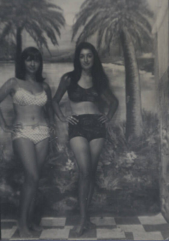 Untitled [Two women stand with hands on hips, beach wallpaper in background, checkered floor]