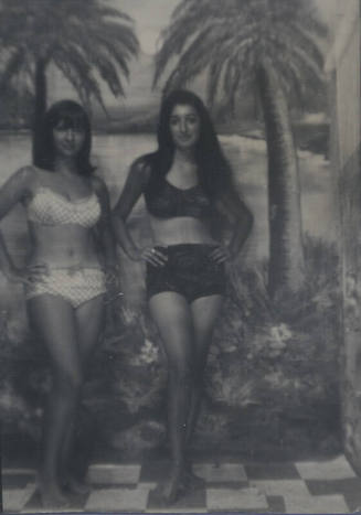 Untitled [Two women stand with hands on hips, beach wallpaper in background, checkered floor]