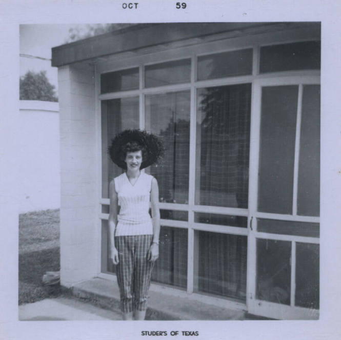 Untitled [Woman stands, hands on either sides of body, glass windows in the background]
