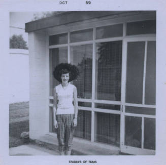 Untitled [Woman stands, hands on either sides of body, glass windows in the background]