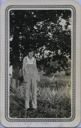 Untitled [Woman stands on field, hands by sides, wears overalls]