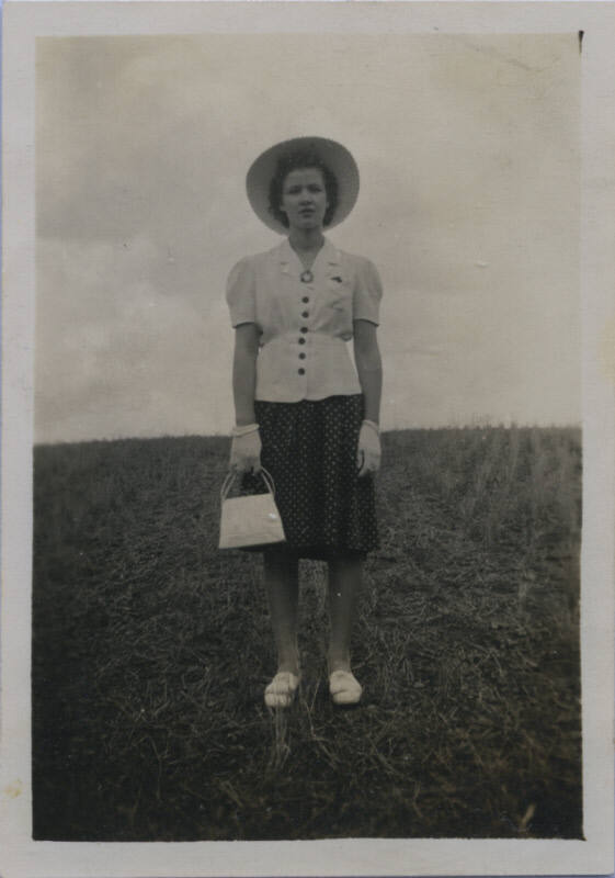 Untitled [Woman stands on field, holds purse in one hand]