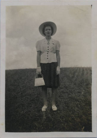 Untitled [Woman stands on field, holds purse in one hand]