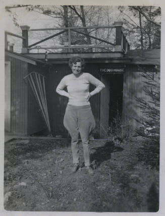 Untitled [Woman stands, hands on hips, house that reads THE DOG HOUSE in background]