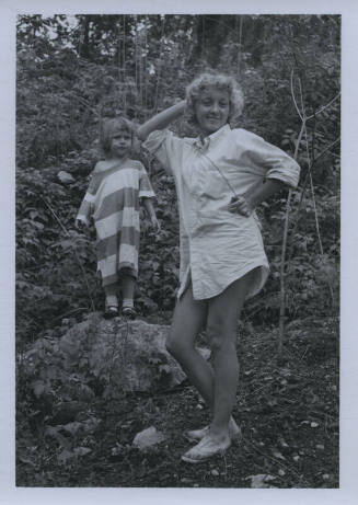 Untitled [Woman stands on hill, hands on hip and head, child in striped shirt by her side]