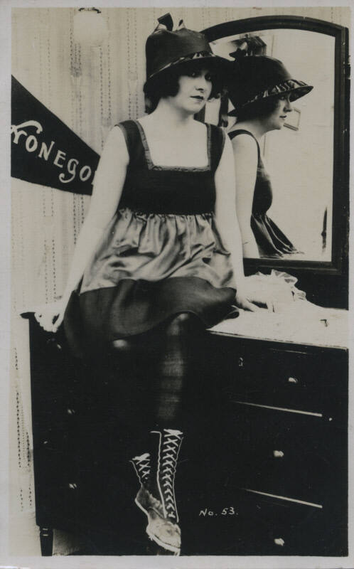 Untitled [Woman sits on dresser, her reflection in the background mirror]