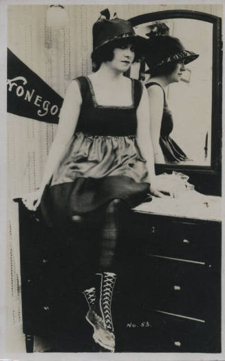 Untitled [Woman sits on dresser, her reflection in the background mirror]
