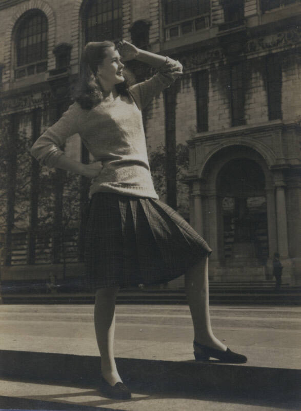 Untitled [Woman looks out, one hand on hip, one above head, places foot on curb]