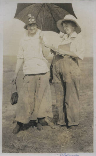 Untitled [Two women stand in field, hold umbrella and sharpen knife]