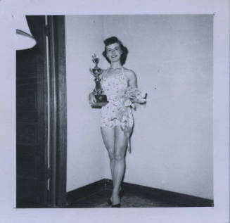 Untitled [Woman stands, holds trophy and flowers on both hands]