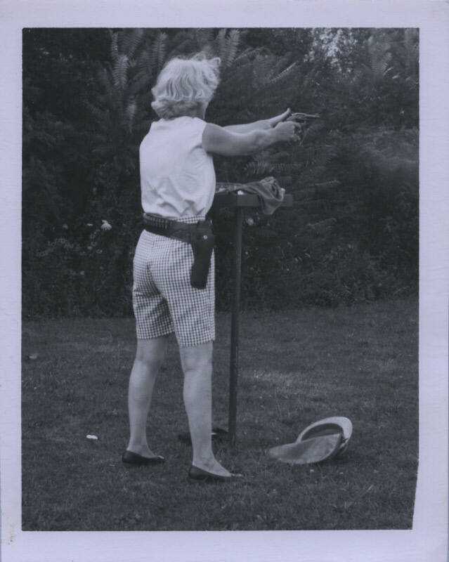 Untitled [Woman stands away from camera, holds up gun]