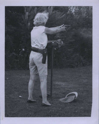 Untitled [Woman stands away from camera, holds up gun]