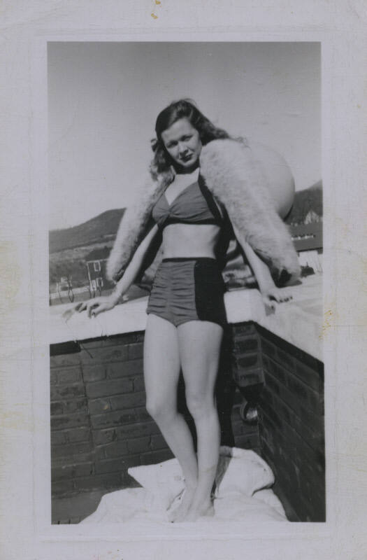 Untitled [Woman stands on rooftop, places hands on either sides of ledge]