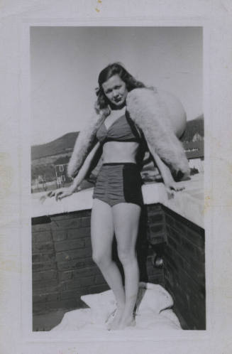 Untitled [Woman stands on rooftop, places hands on either sides of ledge]