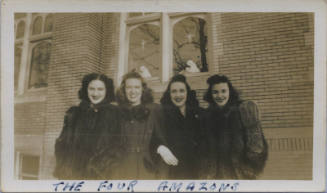 Untitled [Four women stand outside building, religious motifs in background windows]