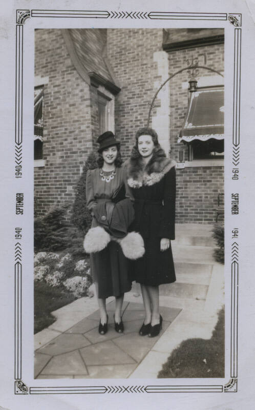 Untitled [Two women stand side by side, brick house in background]
