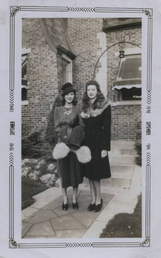Untitled [Two women stand side by side, brick house in background]
