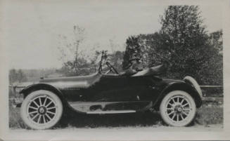Untitled [Woman sits in car's driver's seat, looks sideways to face camera]