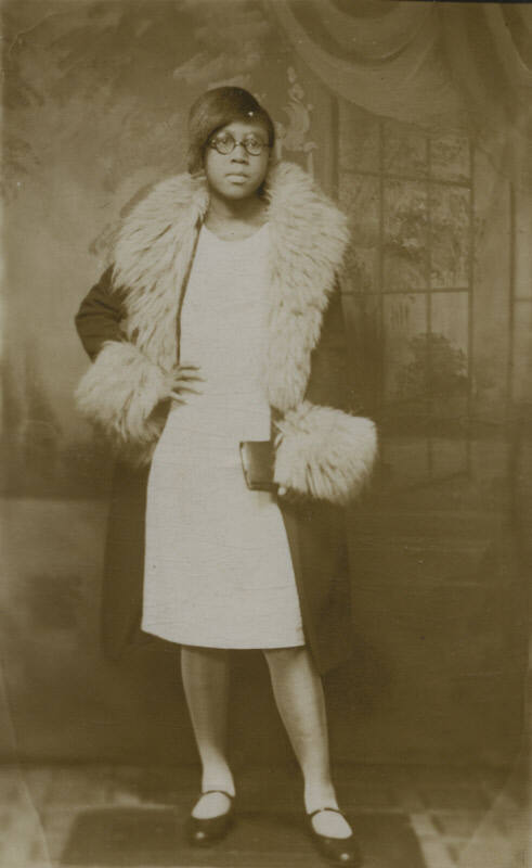 Untitled [Woman stands, hands on waist, living room wallpaper in background]