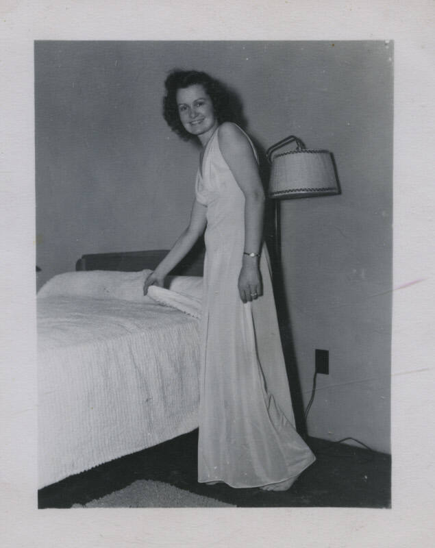Untitled [Woman stands by bed, holds covers]