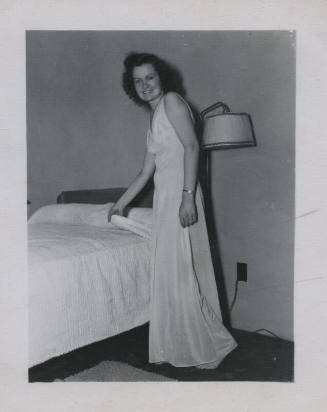 Untitled [Woman stands by bed, holds covers]