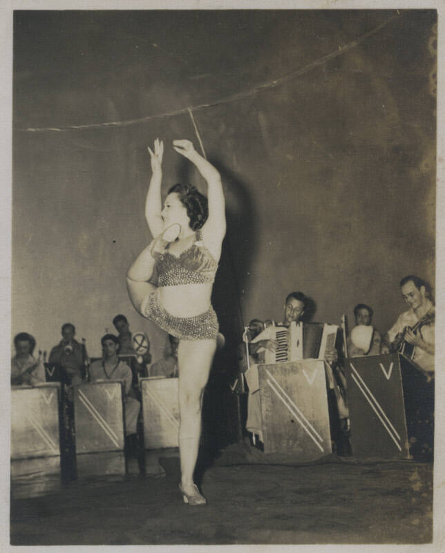 Untitled [Woman stands, raises arms, leg bent behind body and instruments being played in the background]