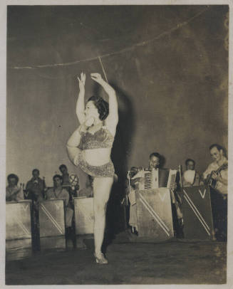 Untitled [Woman stands, raises arms, leg bent behind body and instruments being played in the background]