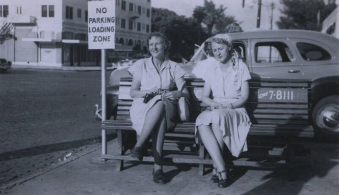 Untitled [Two women sit on bench, sign that reads No Parking Loading Zone in background]