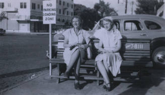 Untitled [Two women sit on bench, sign that reads No Parking Loading Zone in background]
