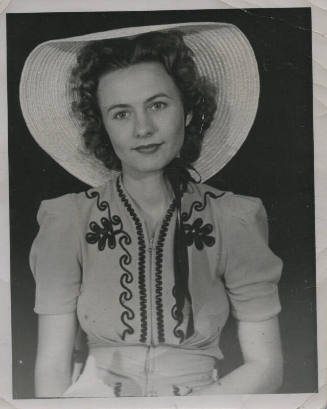 Untitled [Woman sits, wears embroidered shirt and round hat]