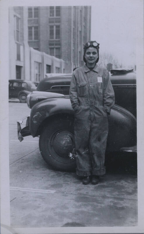 Untitled [Woman stands against car, wears jumpsuit, hands in pockets]
