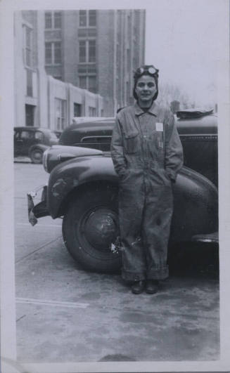 Untitled [Woman stands against car, wears jumpsuit, hands in pockets]