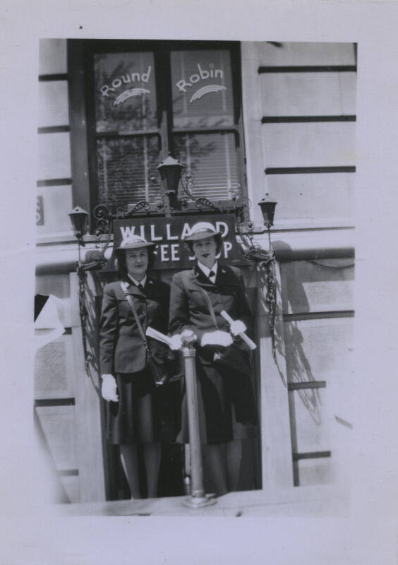 Untitled [Two women stand together, signs that read Round Robin and Willard Coffee Shop in the background]