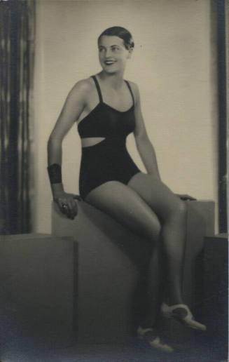 Untitled [Woman sits on crate, looks away, crosses legs]