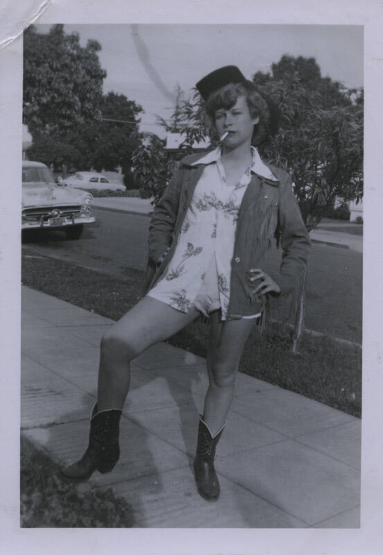 Untitled [Woman stands on street, hand on hip, lifts right leg]