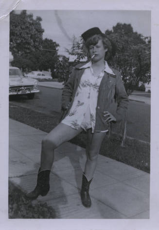 Untitled [Woman stands on street, hand on hip, lifts right leg]