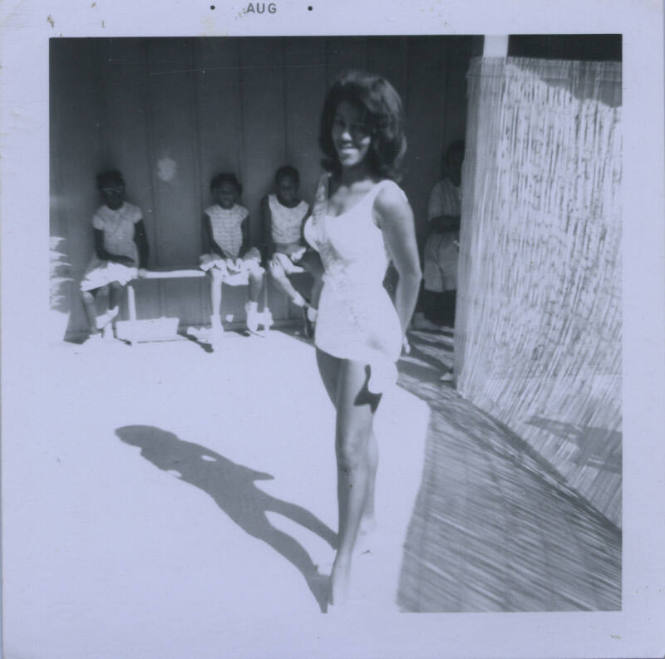 Untitled [Woman stands, hands behind back, banner across body]